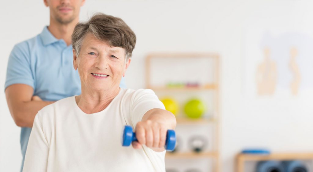 Seniorin streckt lächelnd eine Hantel nach vorne