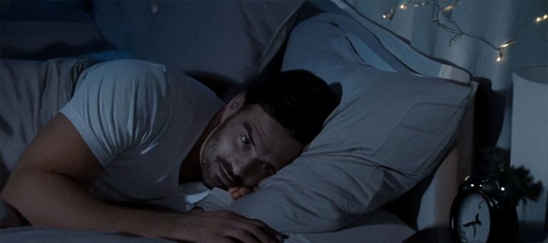 Mann liegt nachts wach in seinem Bett und schaut auf den Wecker